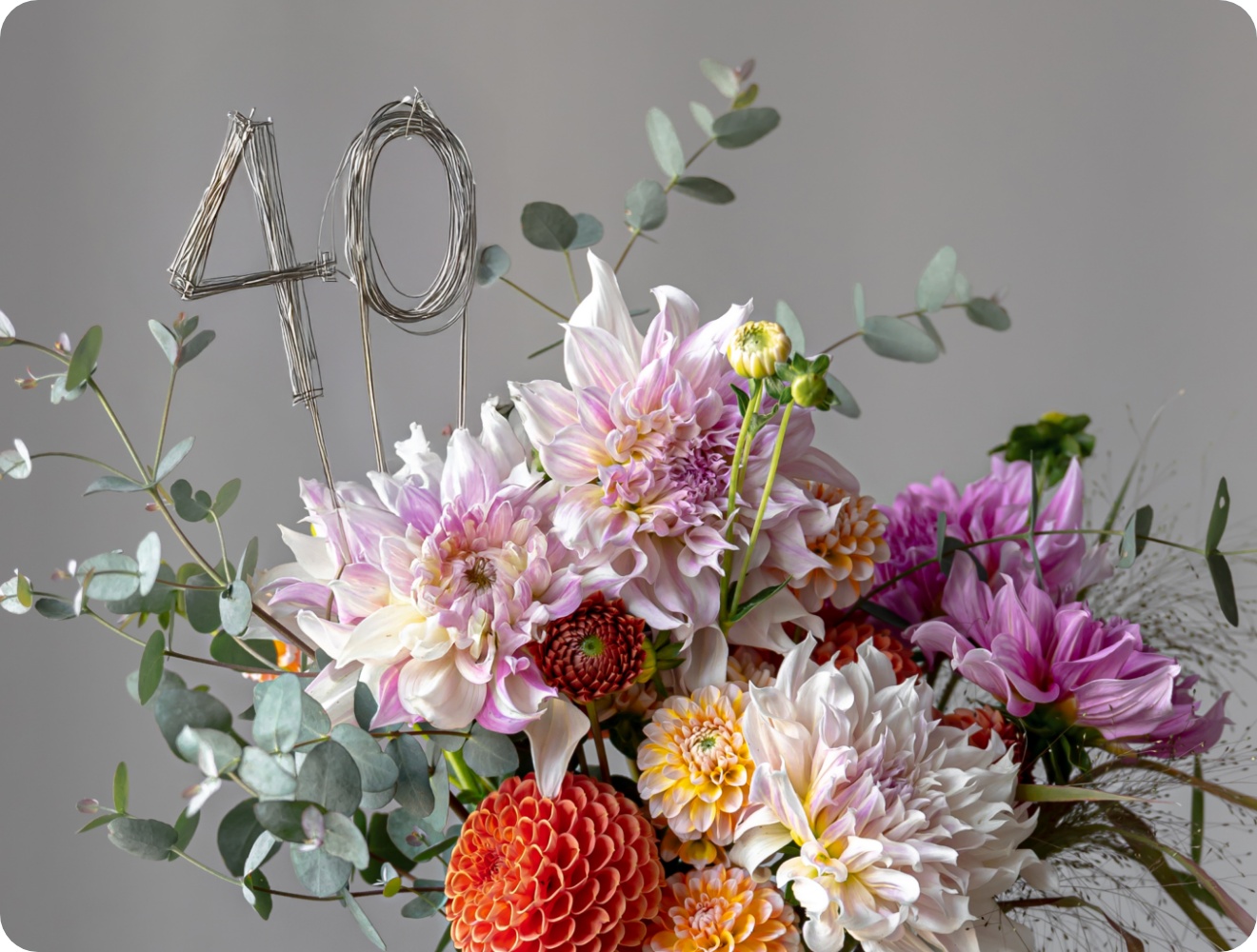 Festlicher Blumenstrauß aus bunten Dahlien, Eukalyptus und Draht-Dekoration mit der Zahl 40 vor grauem Hintergrund..
