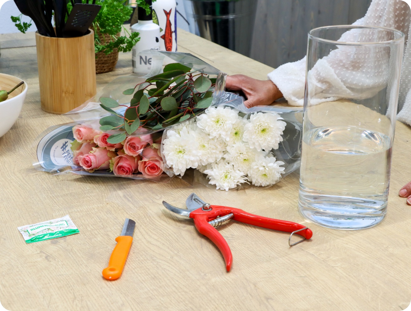 Frische Blumen, Vase mit Wasser und Materialien auf einem Tisch.