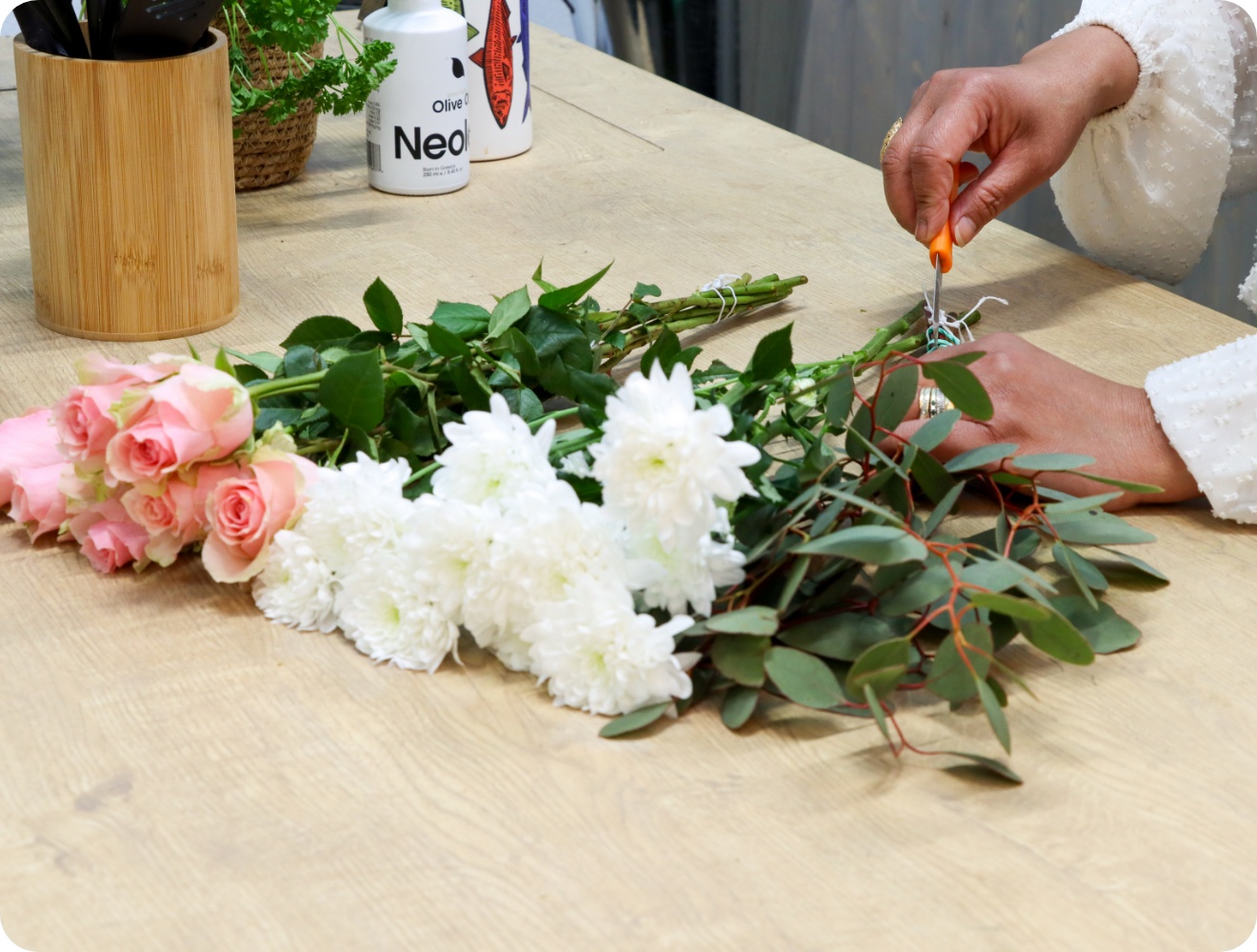 Person entfernt die Blätter von rosa Rosen und weißen Chryanthemen, die auf einer Tischplatte liegen.
