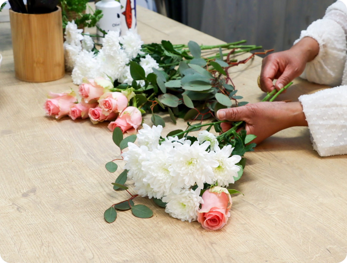 Person sortiert rosa Rosen und weiße Chrysanthemen auf einer Tischplatte.