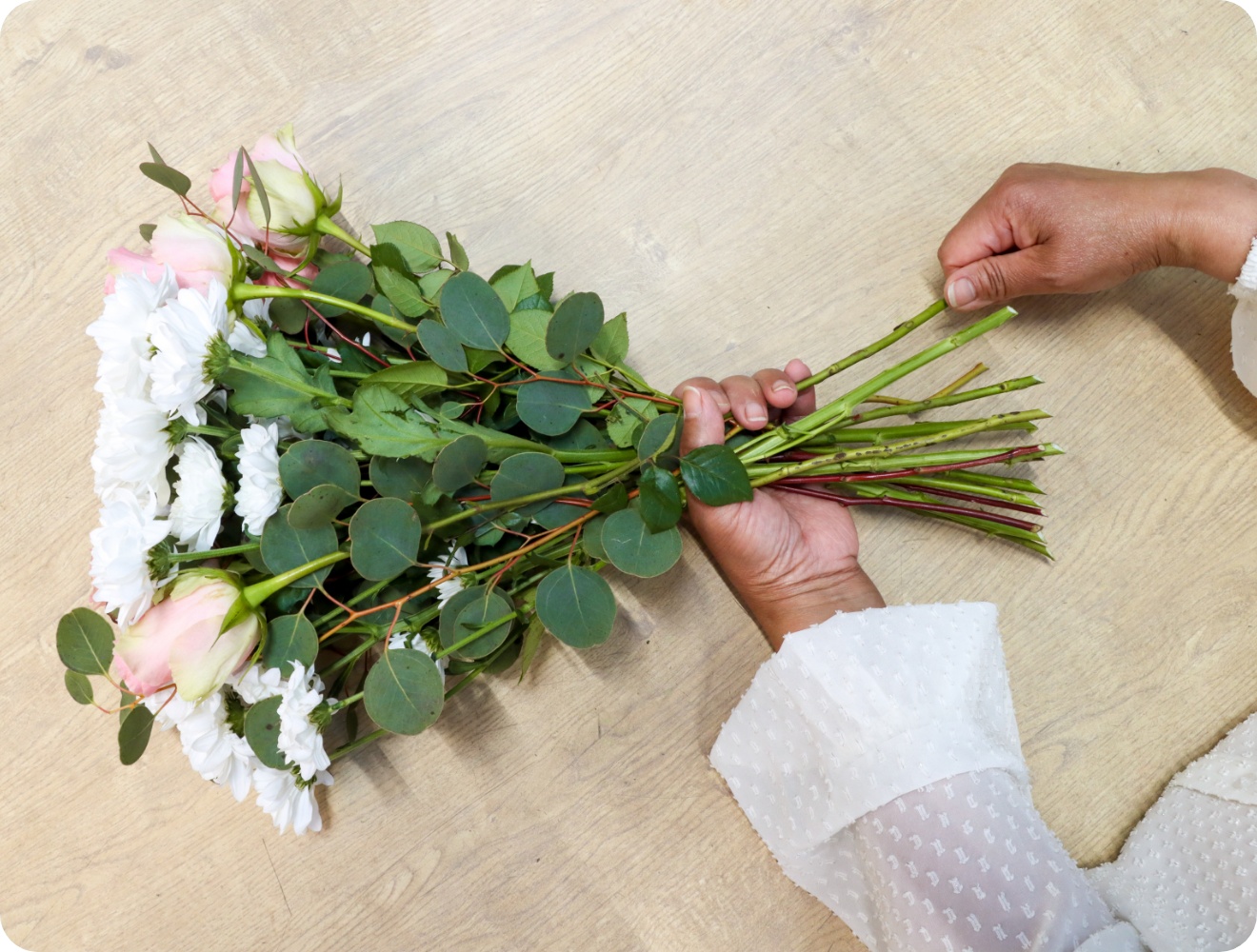 Person bindet Blumenstrauß an den Stielen zusammen.