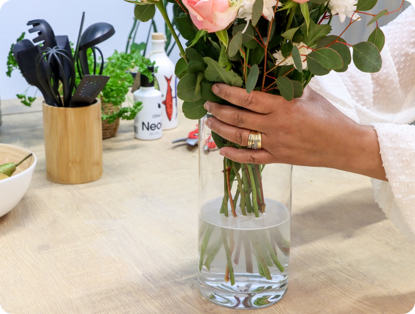 Person stellt gebundenen Blumenstrauß in eine mit Wasser gefüllte Vase.