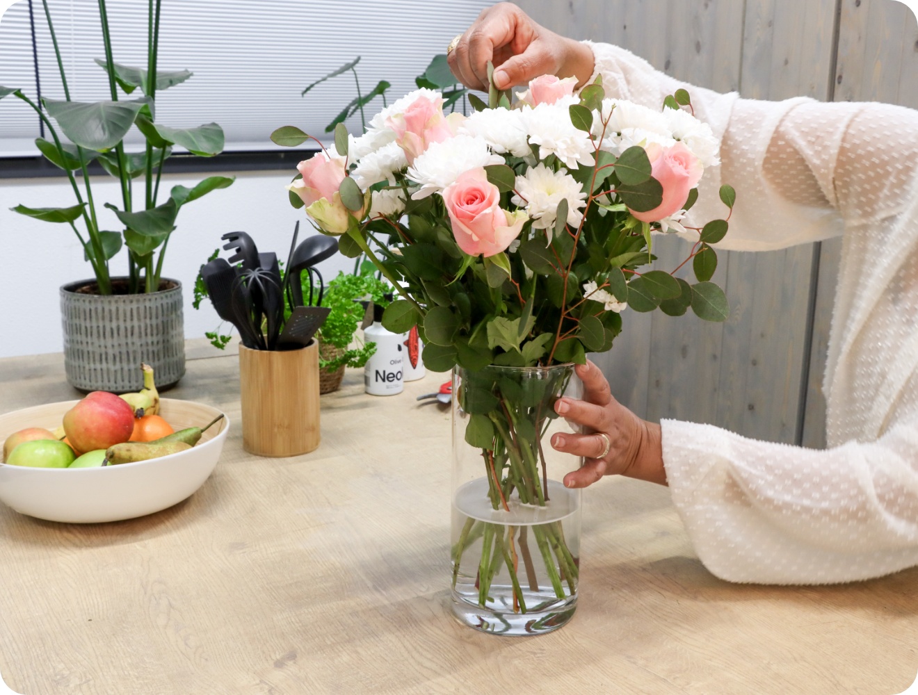 Person rückt Blumenstrauß der in einer Vase steht zurecht.