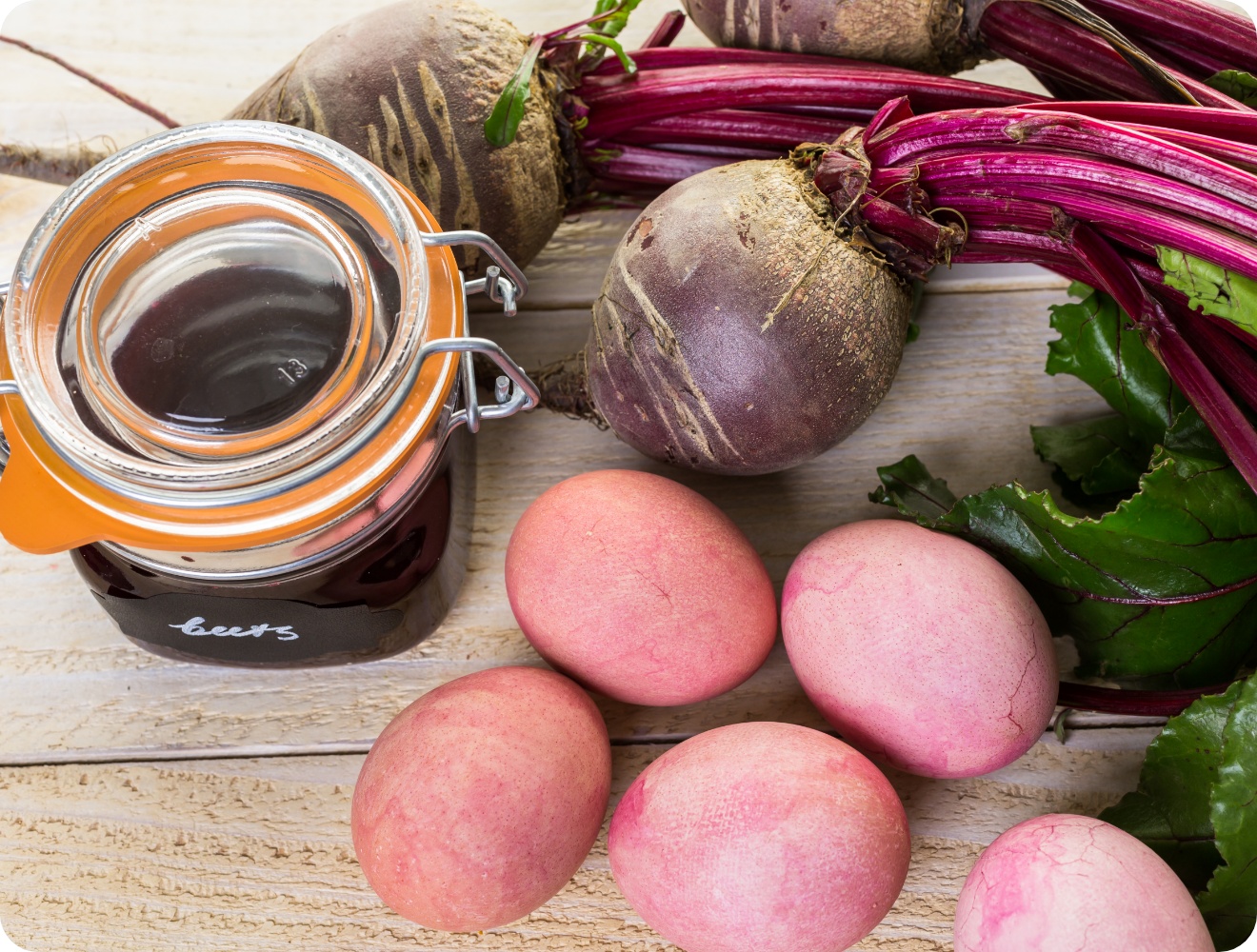 Natürlich gefärbte rosa Ostereier, Rote Bete und ein Glas Rote-Bete-Farbsud auf rustikalem Holztisch.
