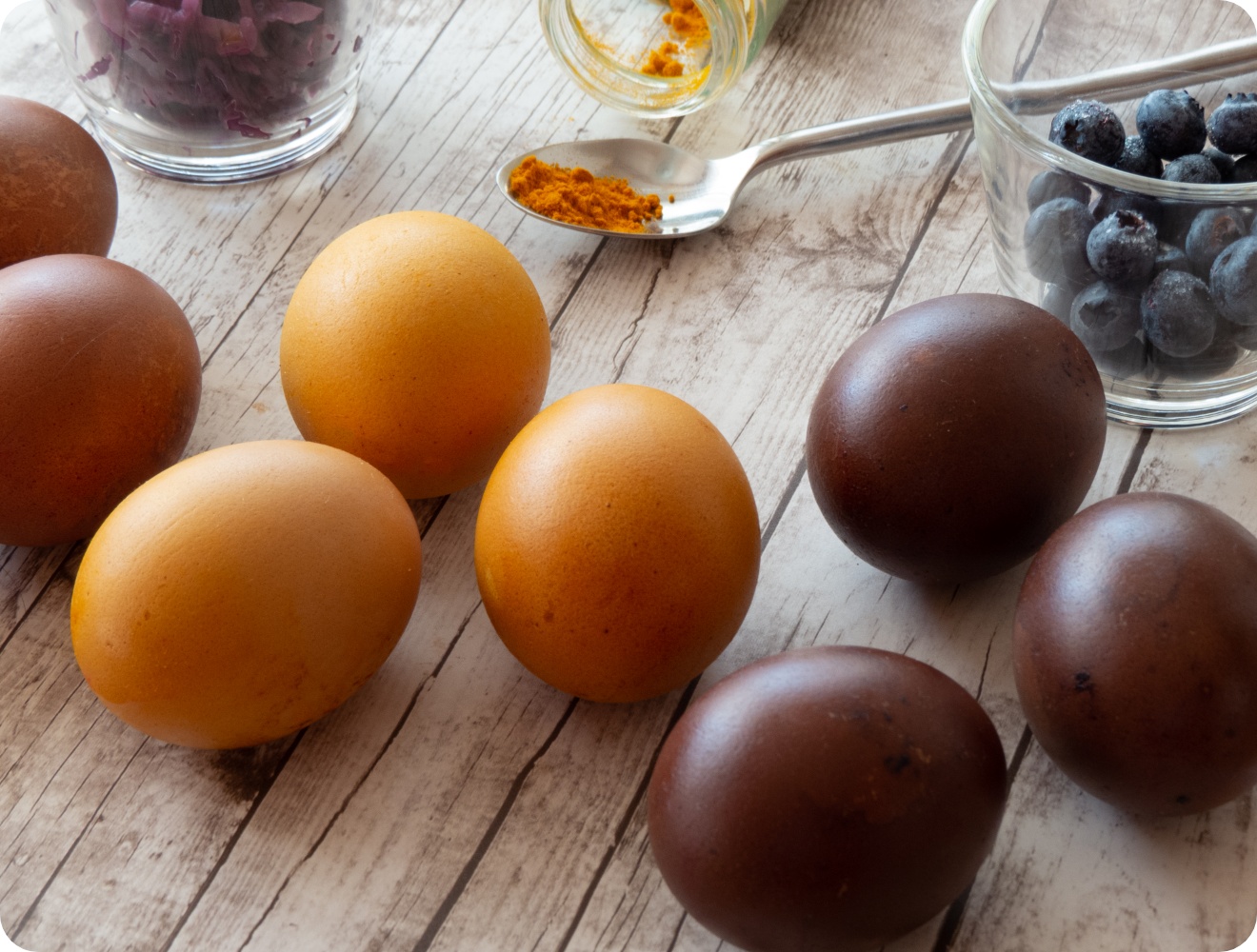 Natürlich gefärbte Ostereier in Gelb und Dunkelbraun mit Kurkuma, Rotkohl und Blaubeeren auf rustikalem Holztisch arrangiert.