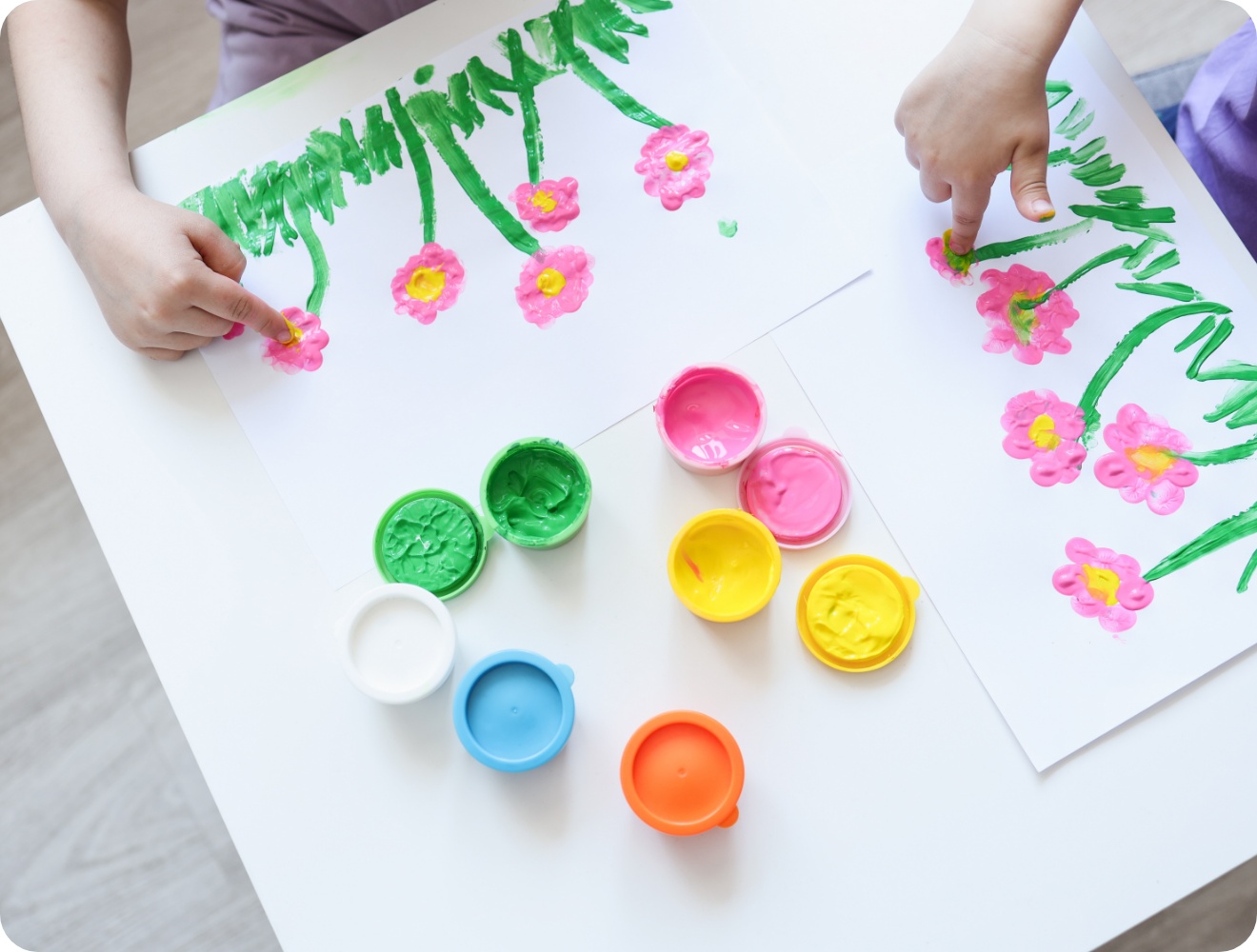 Kinder malen bunte Blumen mit Fingerfarben auf Papier, Bastelaktion zum Muttertag am Tisch.