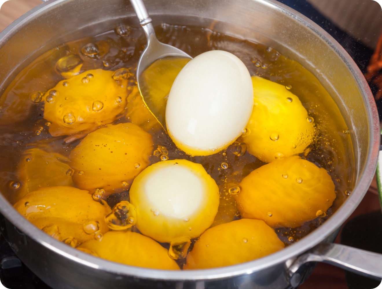 Kochtopf mit sprudelndem Wasser, in dem ungeschälte Eier gelb gefärt werden.