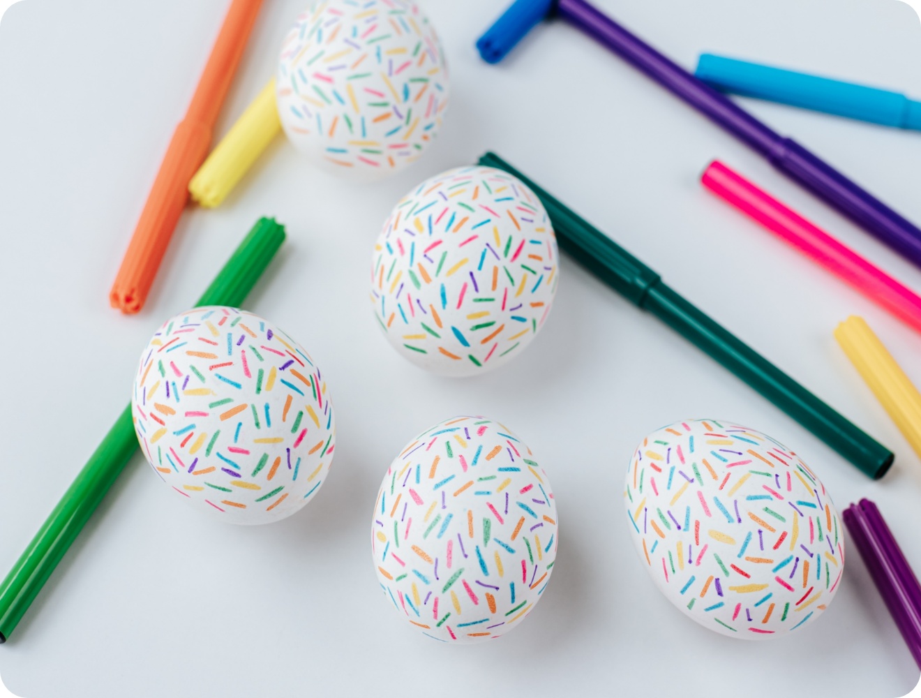 Weiße mit Filzstiften bemalte Ostereier mit bunten Strichmustern.