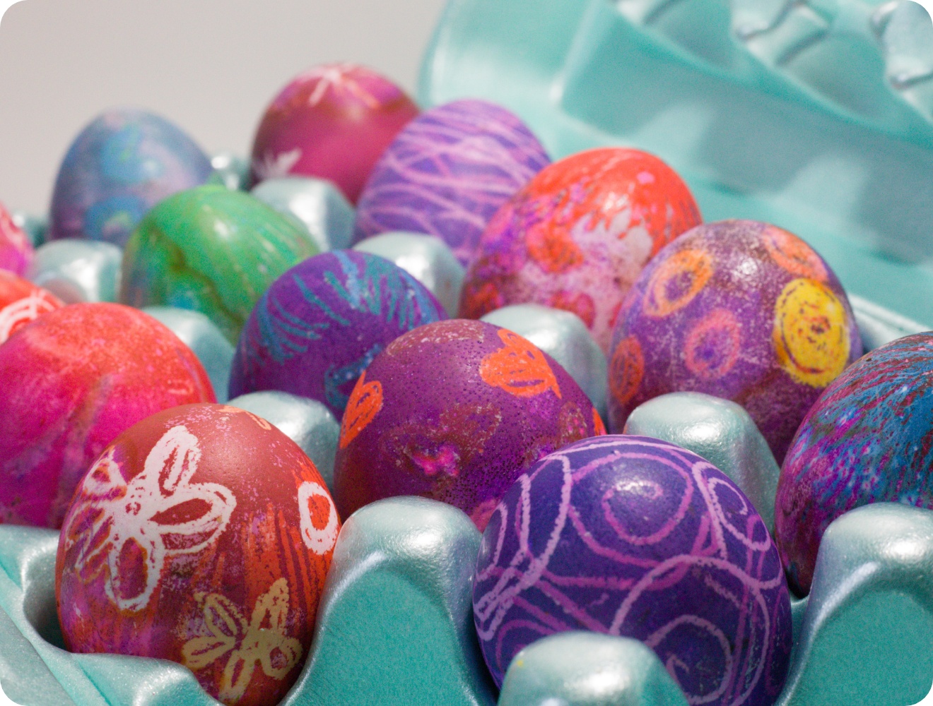 Farbenfroh verzierte Ostereier mit Mustern in einer türkisfarbenen Eierverpackung, kreativ gestaltet in Rot, Lila und Blau.