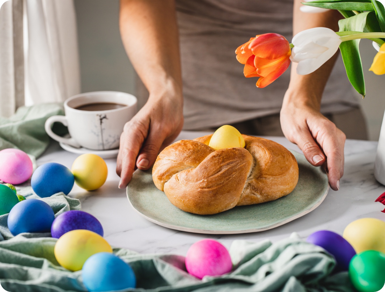 Eine Person stellt einen Hefezopf, geformt als Osternest mit einem Osterei in der Mitte, auf den Tisch.