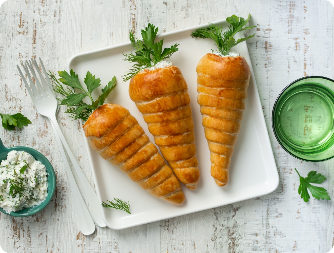 Herzhaft gefüllte Teigkarotten in Möhrenform mit Dill und Petersilie, stilvoll auf Holz serviert.