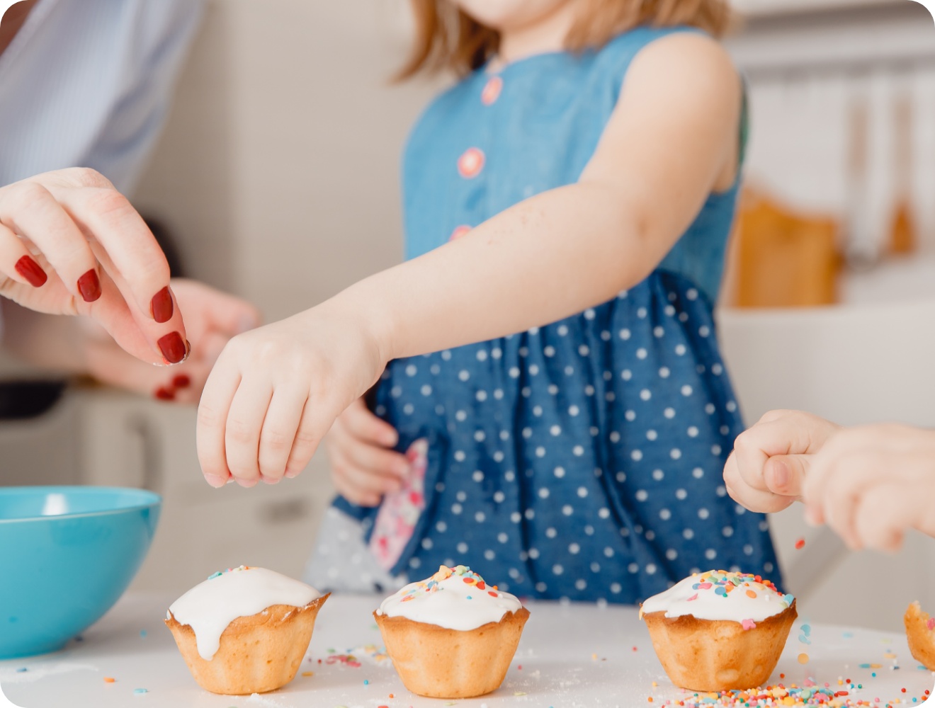 Kinder dekorieren Muffins mit Zuckerguss und bunten Streuseln beim gemeinsamen Osterbacken in der Küche.
