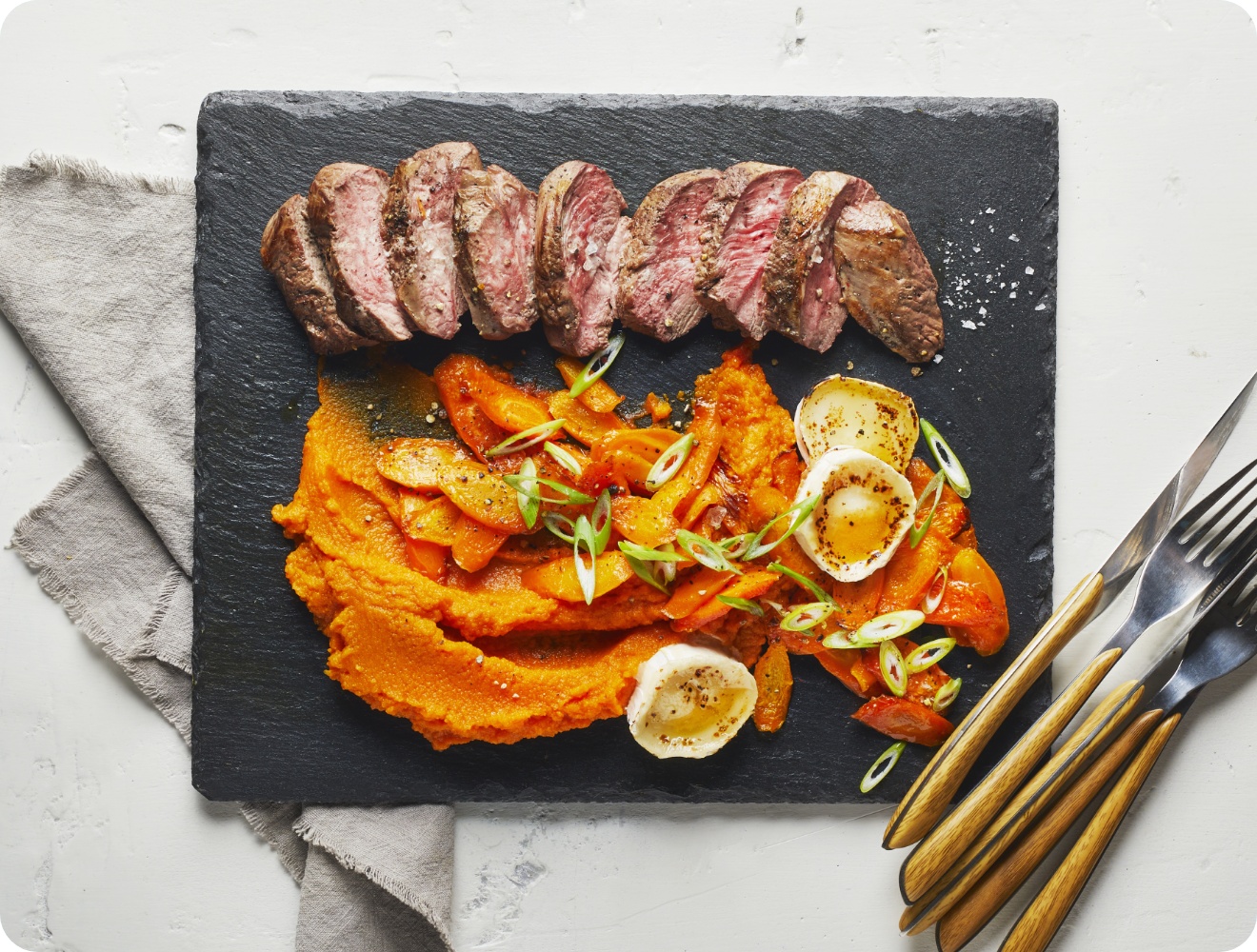 Als Hauptgericht zu Ostern liegt ein gebratenes Lammsteak aufgeschnitten und mit etwas Möhrenpüree als Beilage auf einer Schieferplatte