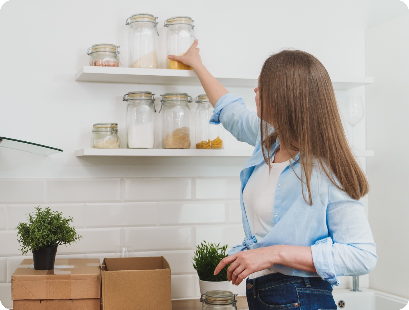 Frau in einer hellen Küche immt ein Glas mit Lebensmitteln von einem weißen Wandregal.