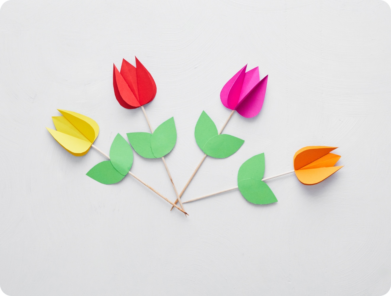 Bunte Tulpen aus Papier mit grünen Blättern auf Holzstäbchen, kunstvoll arrangiert auf weißem Hintergrund.