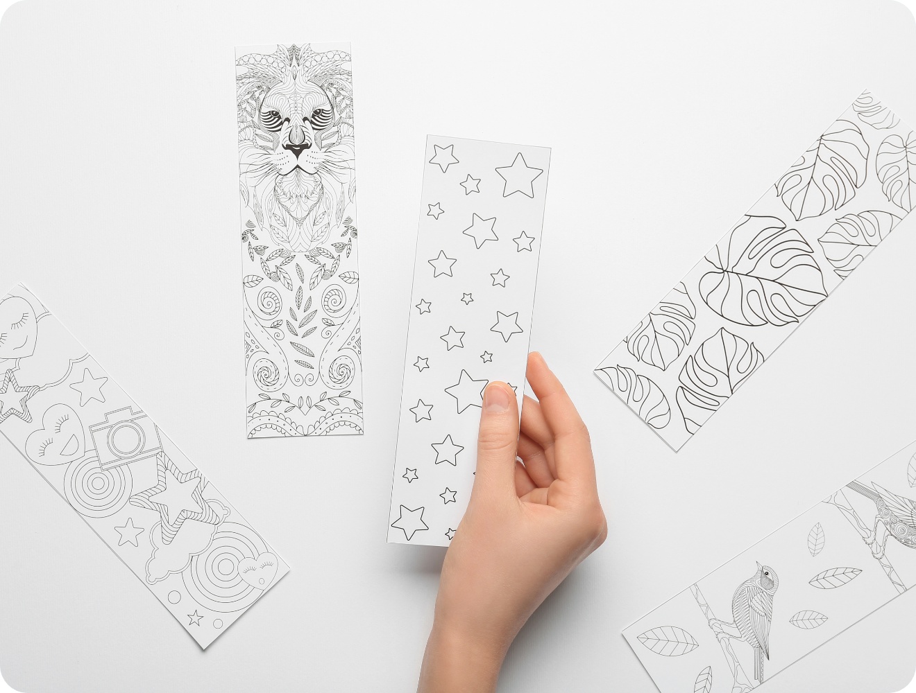 Hand hält ein Lesezeichen mit Sternenmuster. Umgeben von weiteren schwarz-weißen Lesezeichen mit Tier- und Pflanzenmotiven.