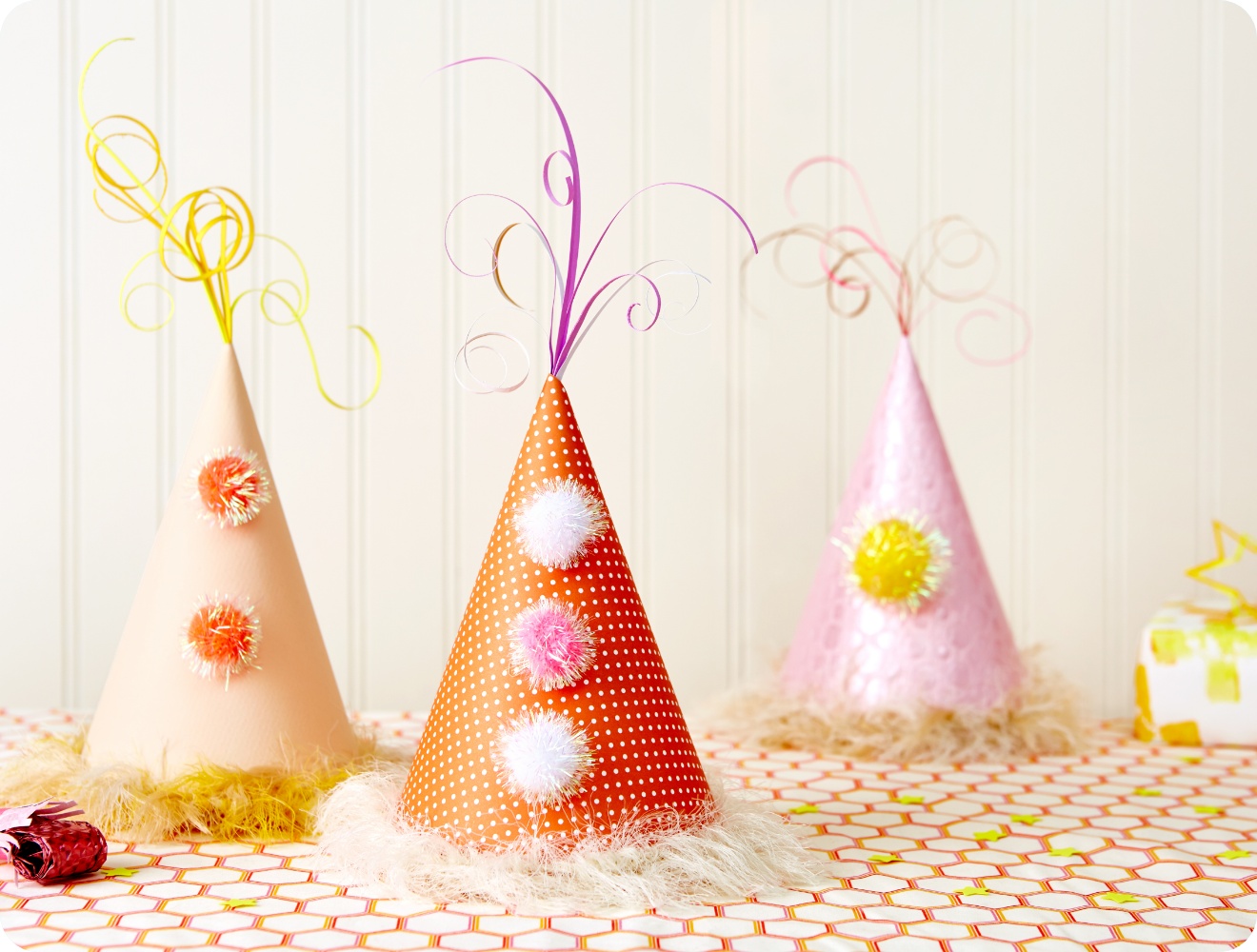 Drei festliche Partyhüte mit Pompons und Lockendekor auf dekoriertem Tisch. Farbenfrohe Geburtstagsdekoration im Hintergrund.