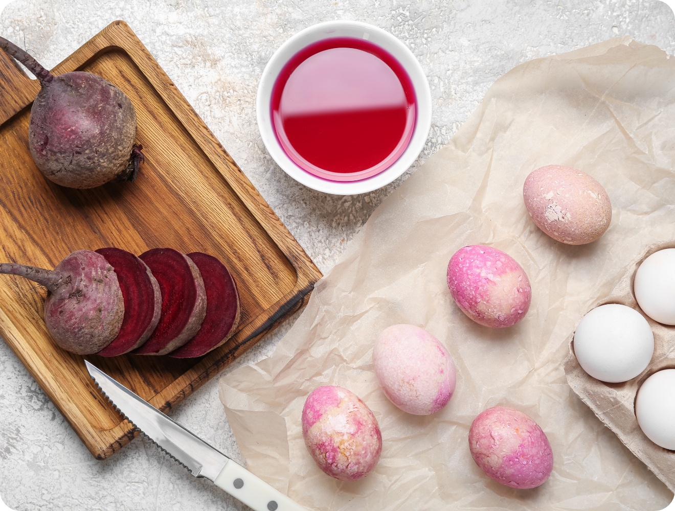 Natürlich gefärbte Ostereier mit Roter Bete auf Pergamentpapier. Daneben geschnittene Rote Bete, Messer und Rote-Bete-Saft.