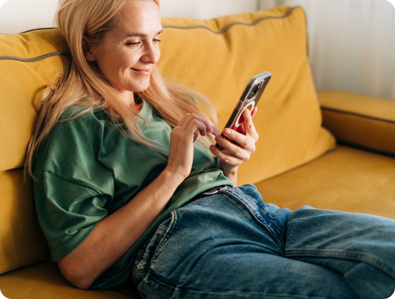Frau in grünem T-Shirt liegt entspannt auf gelbem Sofa und benutzt ihr Smartphone.