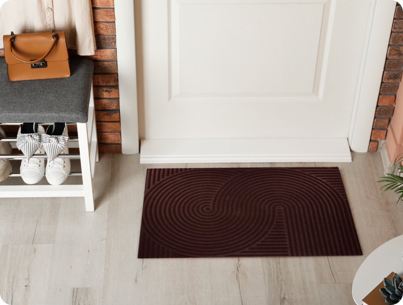 Eingangsbereich mit Welcome-Fußmatte, Schuhregal, grauer Bank und Tasche an der Wand.