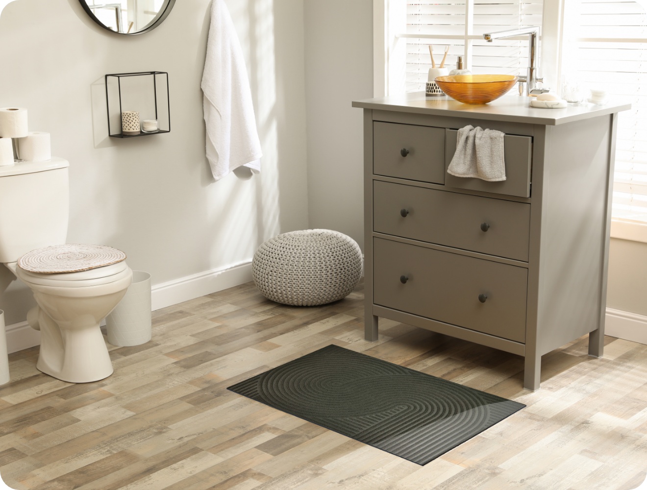 Modernes Badezimmer mit grauem Waschtisch, dunkelgrauer ALDI Fußmatte, Toilette und rundem Hocker.