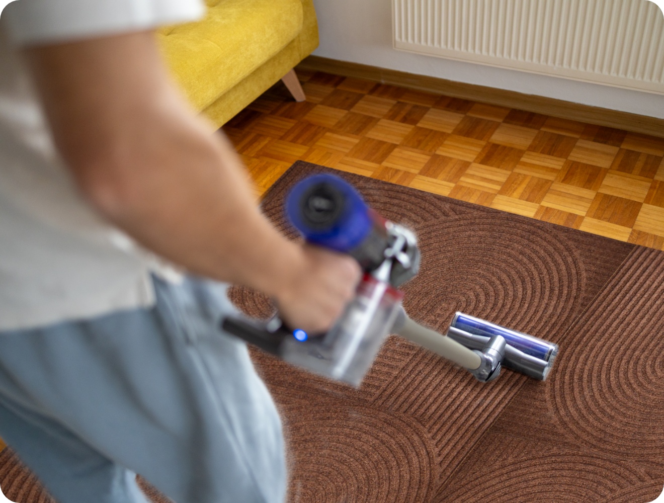 Person saugt mit einem kabellosen Staubsauger als Teppich zusammengesetzte ALDI Fußmatten in der Farbe Anthrazit in einem Wohnzimmer.