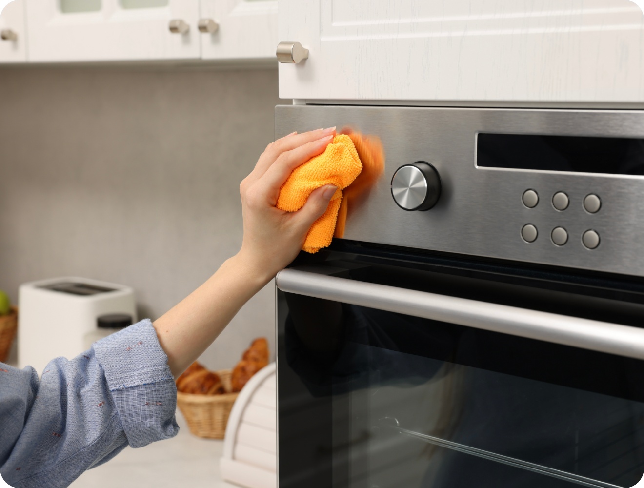 Person reinigt mit einem orangefarbenen Mikrofasertuch die Edelstahlfront eines Backofens.