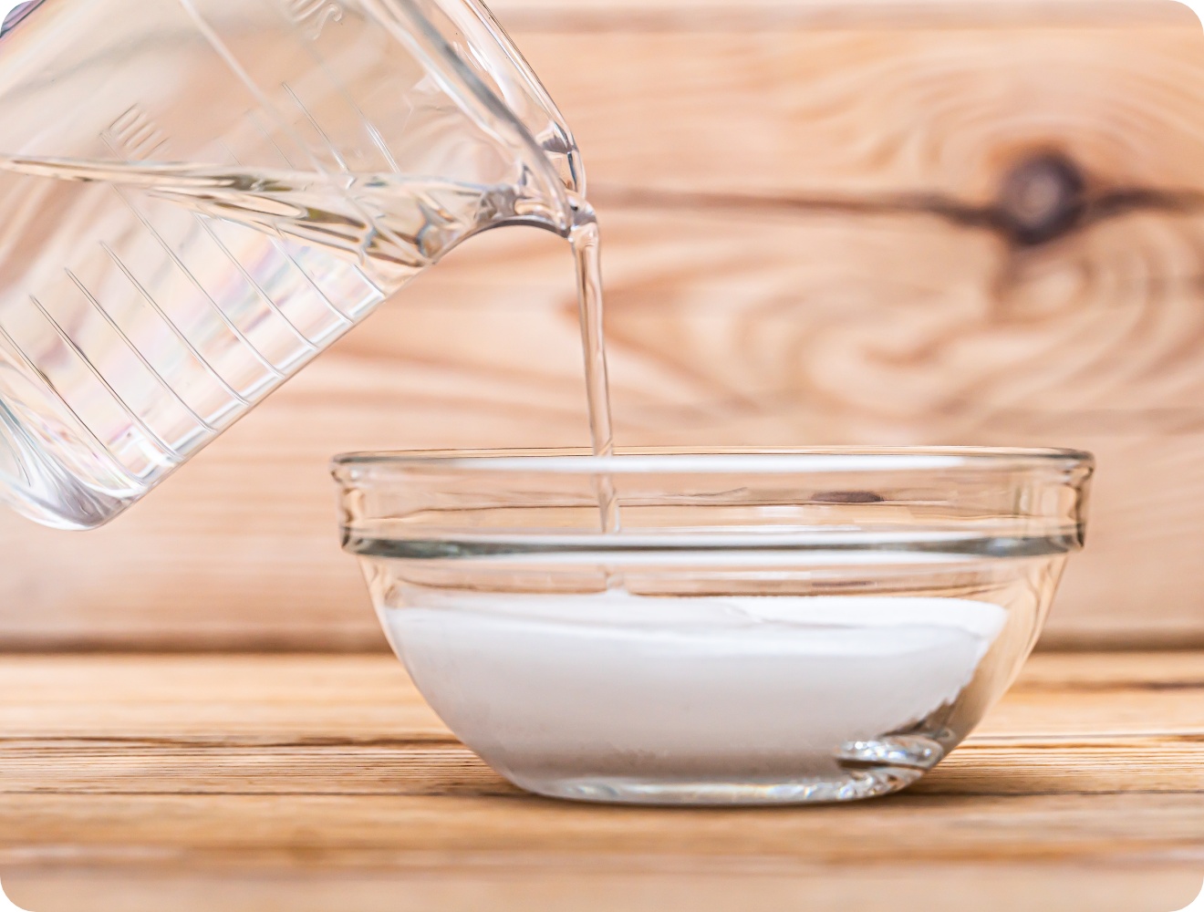 Nahaufnahme wie Essig aus einem Messbecher in eine Glasschale mit Natron gegossen wird.