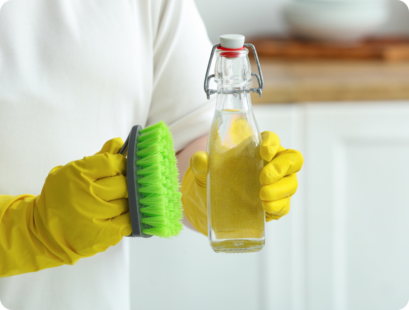 Person mit gelben Gummihandschuhen hält eine grüne Reinigungsbürste und eine Flasche mit selbstgemachtem natürlichem Reiniger.