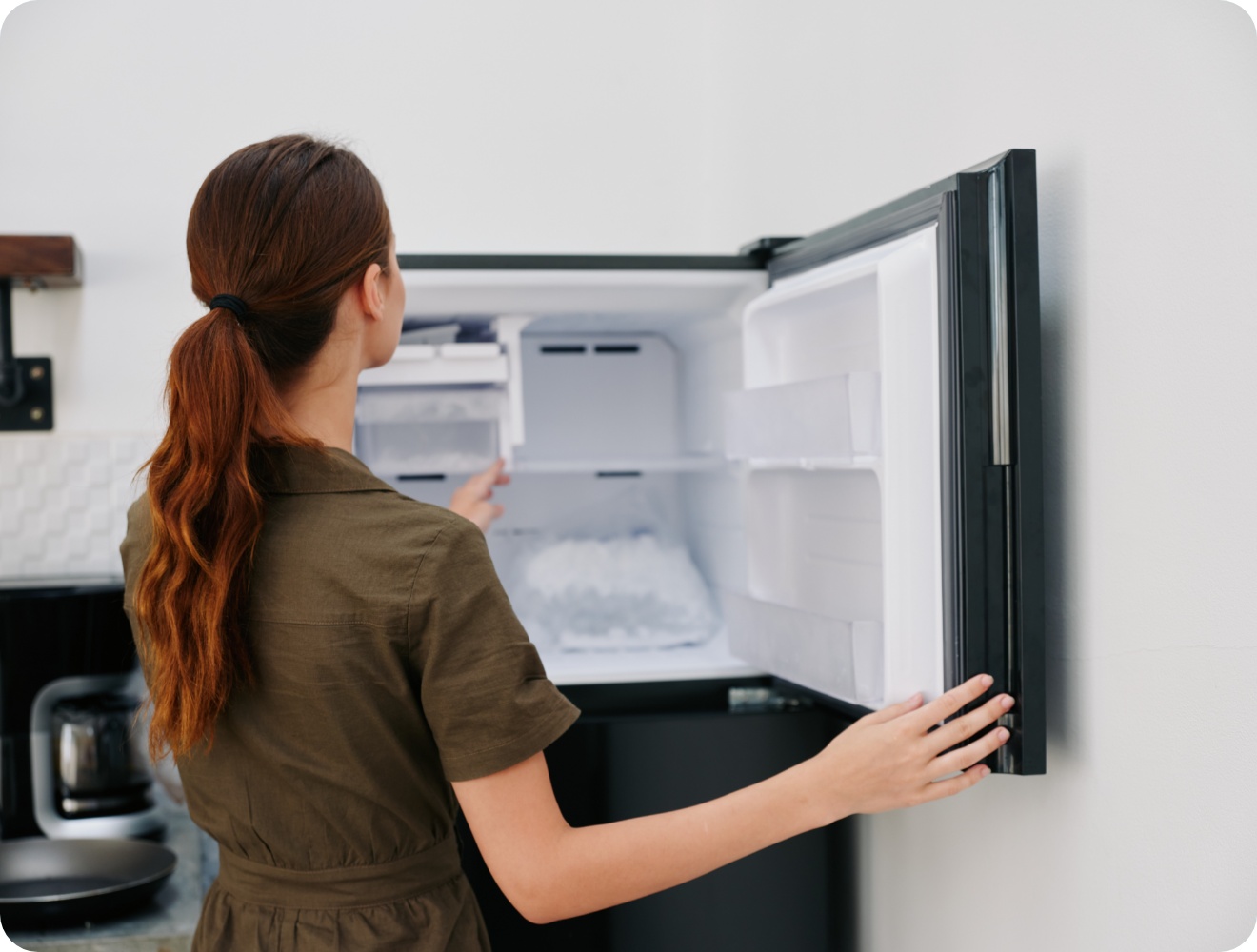 Frau öffnet einen mit Eiswürfeln gefüllten Gefrierschrank in einer modernen Küche.
