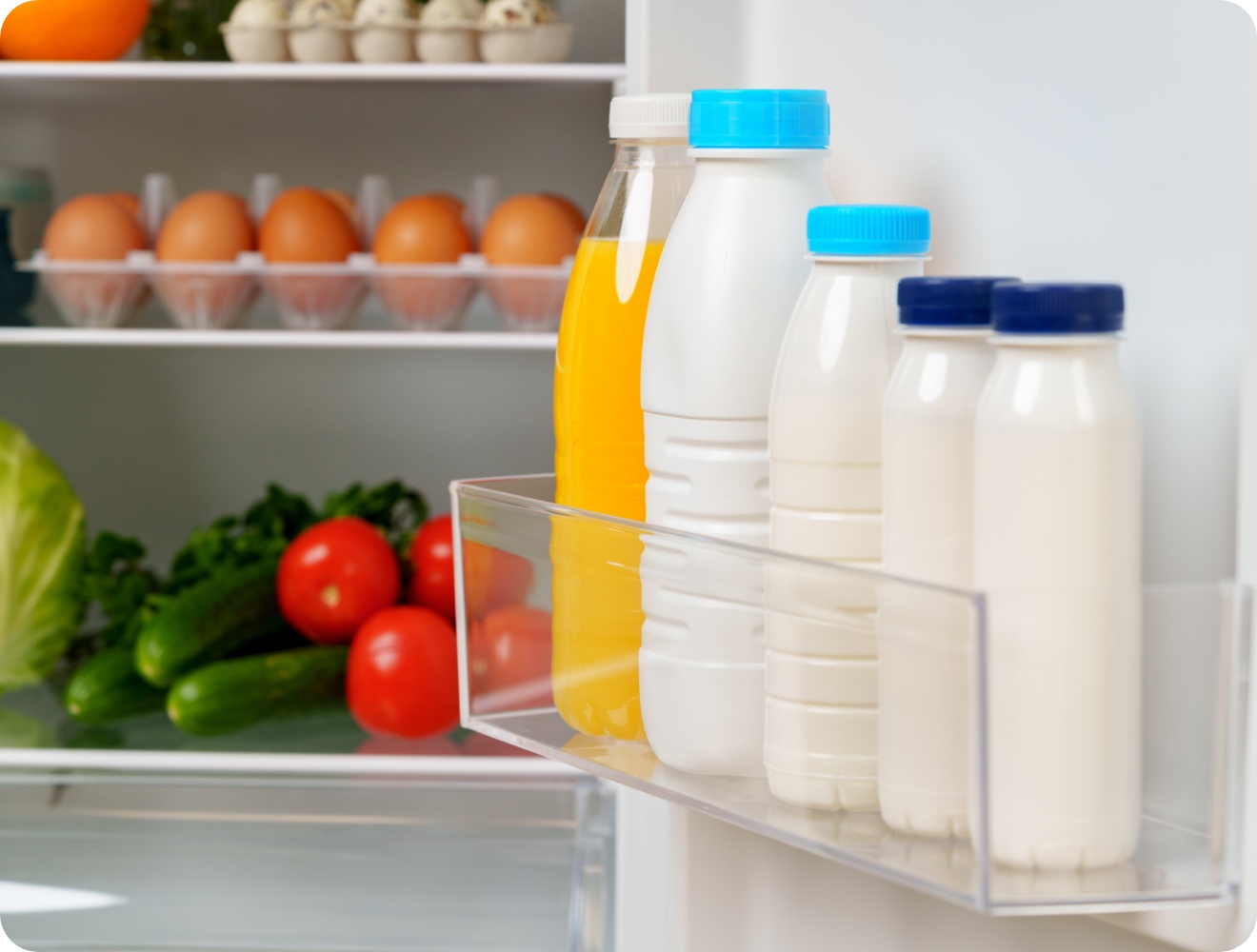 Offener Kühlschrank mit Milch- und Saftflaschen in der Tür, frischen Eiern im Regal sowie Gemüse wie Tomaten und Gurken.