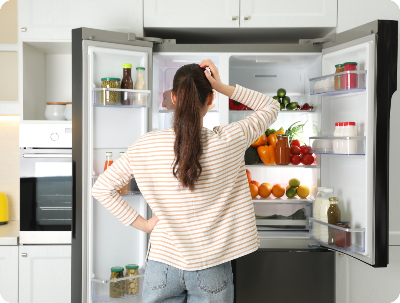 Frau in gestreiftem Pullover steht fragend vor offenem Kühlschrank mit zwei Türen gefüllt mit Lebensmitteln.