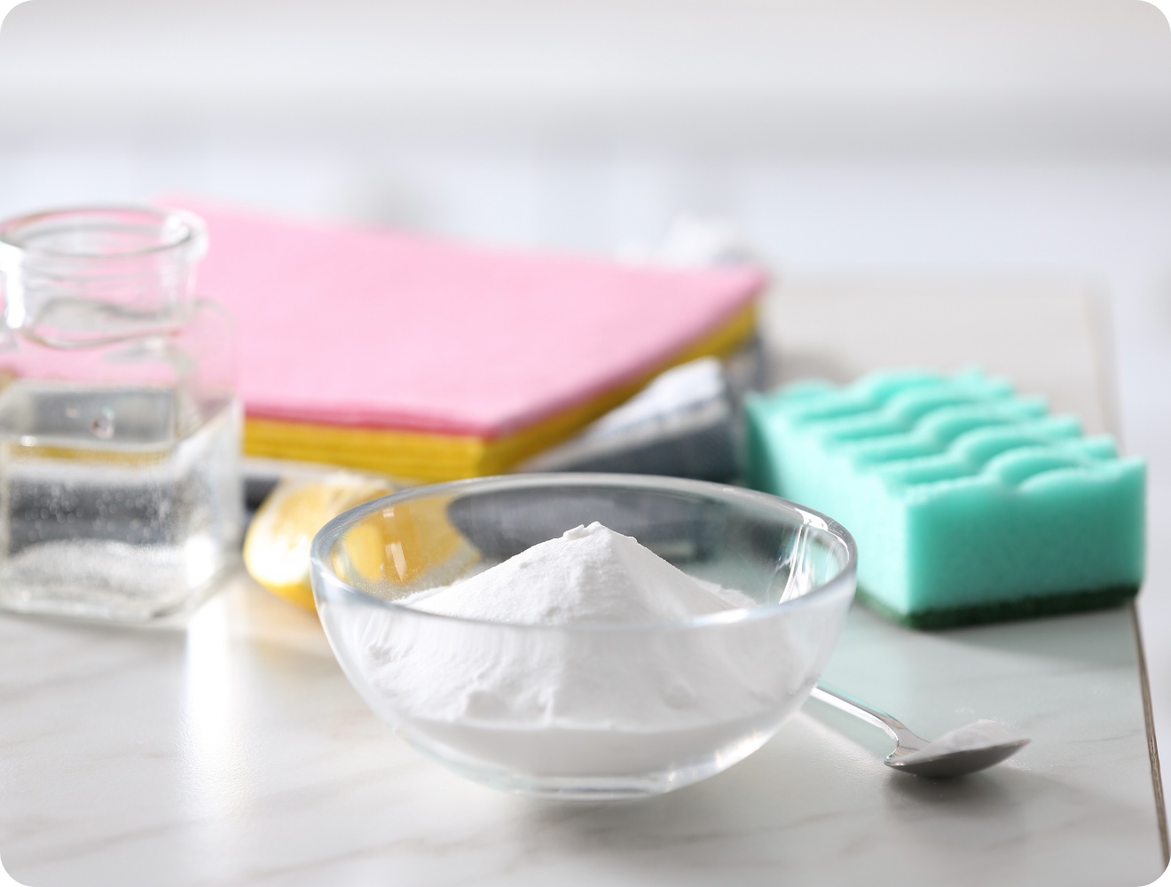 Natron in Glasschüssel, Essigflasche, Zitronenscheibe, Schwämme und Reinigungstücher.