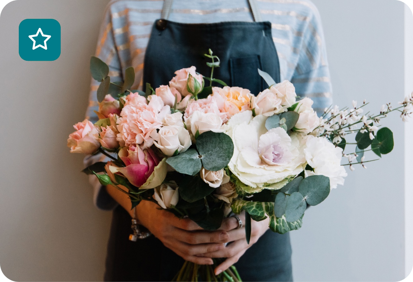 Floristin mit dunkelgrüner Schürze hält Blumenstrauß aus weißen und hellrosafarbenen Blumen.