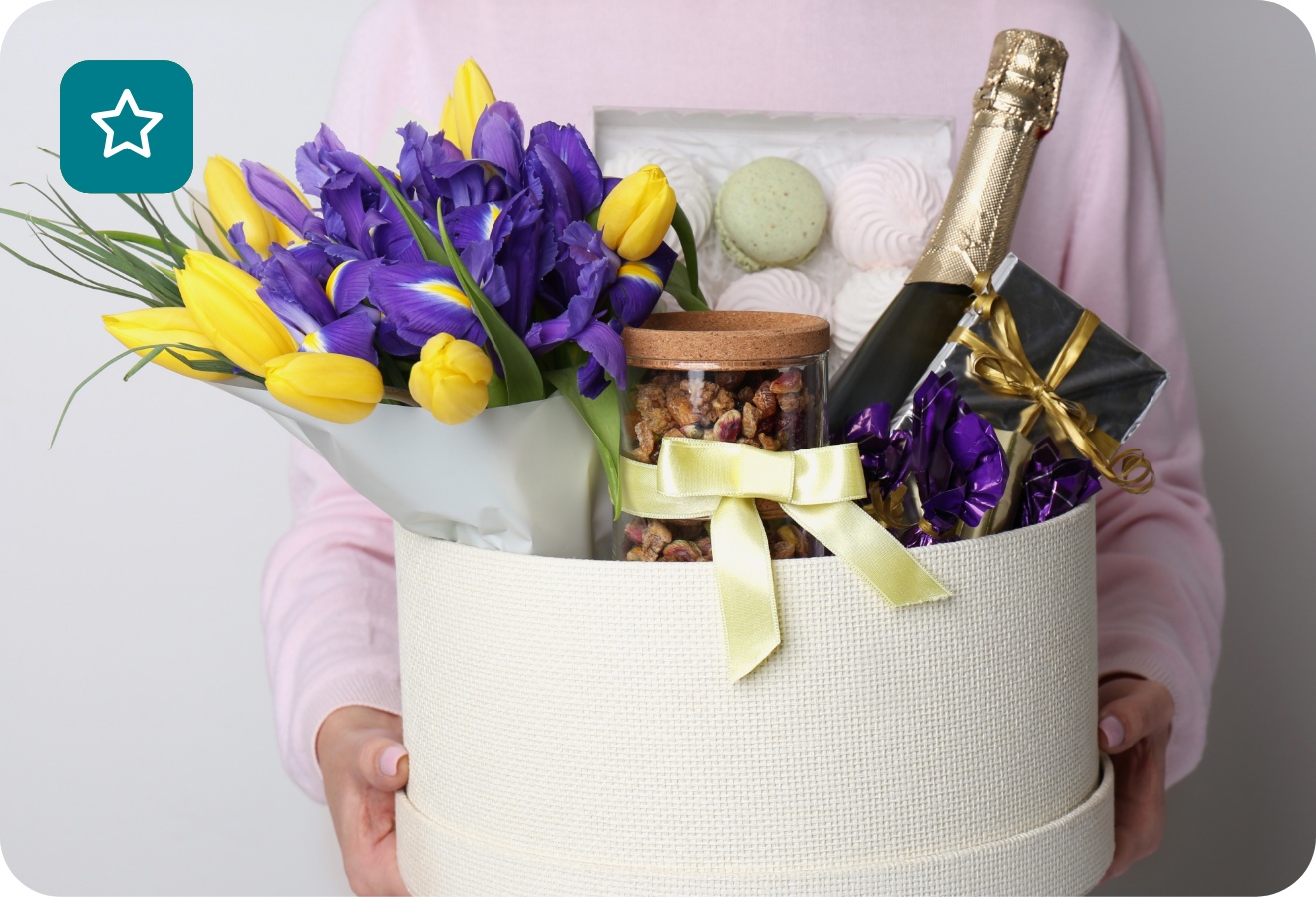 Eine junge Frau hält einen Geschenkkorb mit Sekt, Nüssen, Snacks und Blumen.