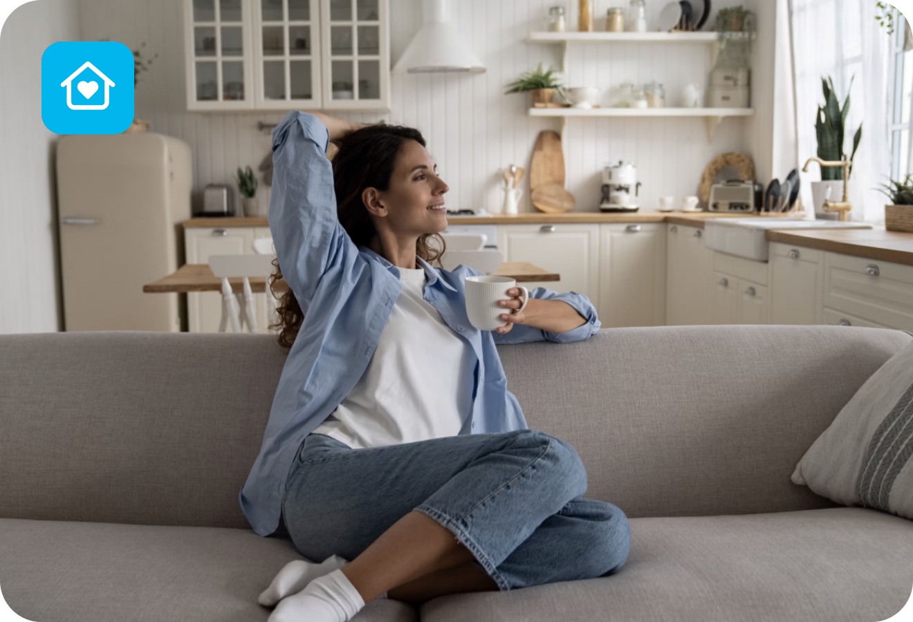 Frau sitzt entspannt auf einem Sofa mit einer Tasse Kaffee in einer hellen aufgeräumten Wohnküche.