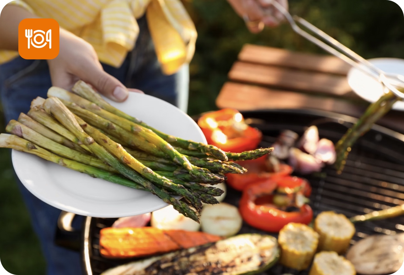 Gegrillter grüner Spargel auf einem Teller. Im Hintergrund verschiedenes gegrilltes Gemüse auf dem Grill.