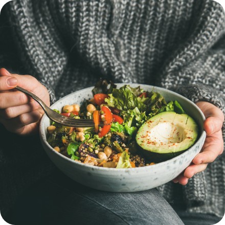 Gabel mit Tofu-Stück über einer farbenfrohen Salatschüssel mit Avocado, Edamame, Pommes und Blattsalat.