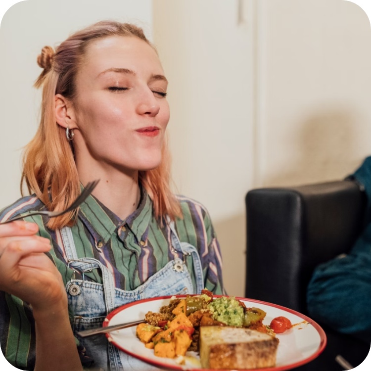 Frau hält einen Teller mit gekochtem Gemüse und Brot in der Hand.
