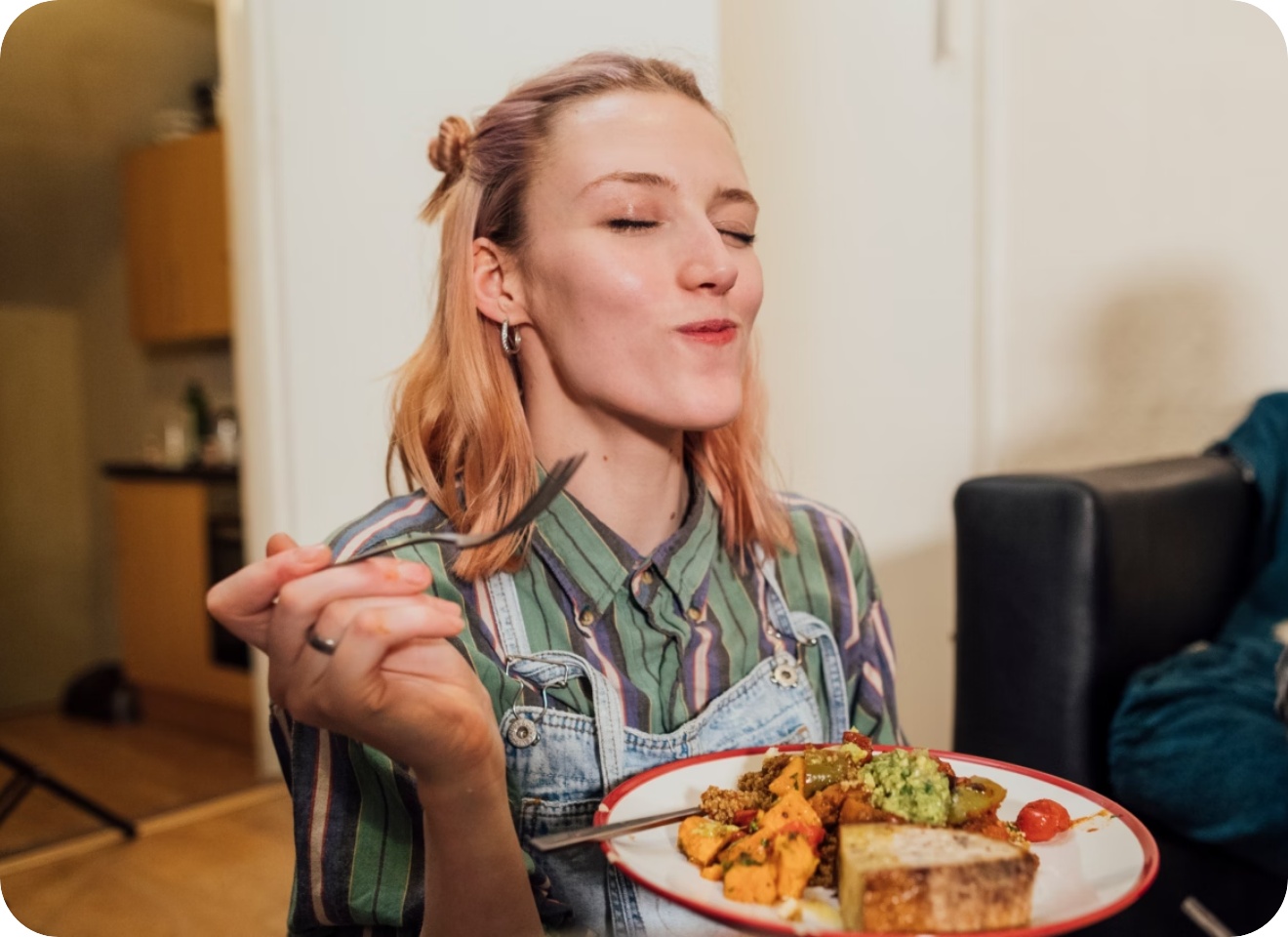 Frau hält einen Teller mit gekochtem Gemüse und Brot in der Hand.