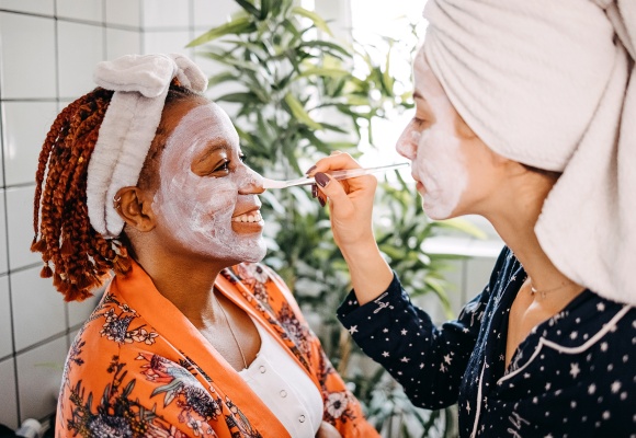 Zwei Freundinnen bepinseln ihre Gesichter mit einer Gesichtsmaske.