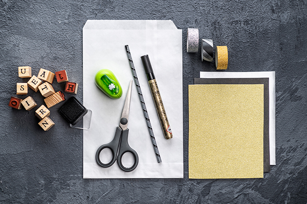Buchstabenstempel, Schere, Stifte, Klebestreifen und Papier auf einem grauen Hintergrund