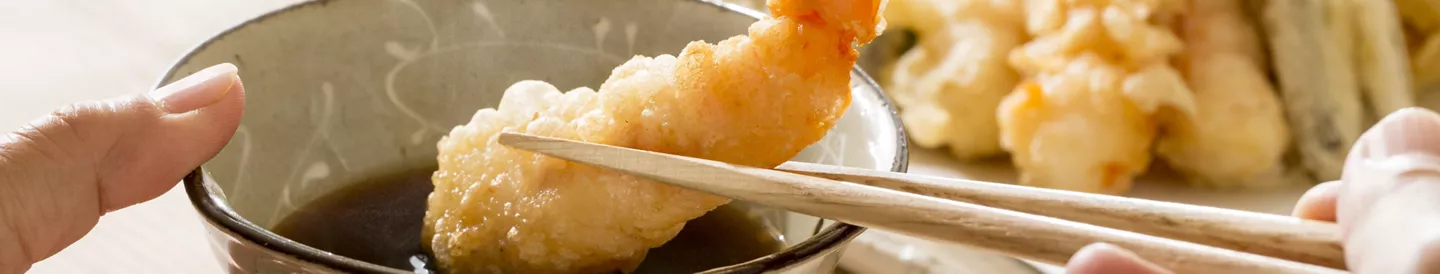 Manos sumergiendo tempura langostinos salsa soja