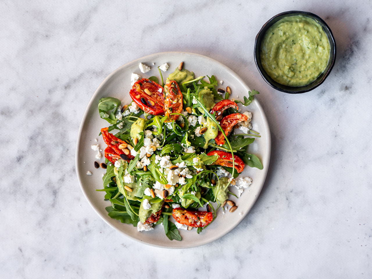 Zomerse salade met rucola, zongedroogde tomaat, feta, geroosterde pijnboompitjes en knalgroene dressing  bij ALDI
