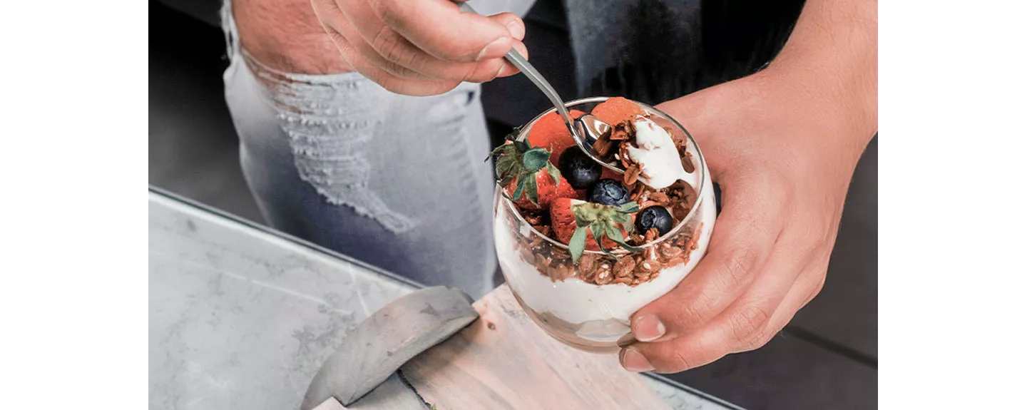 Una persona tomando kéfir con granola y frutas para mostrar las diferencias entre kéfir y yogur