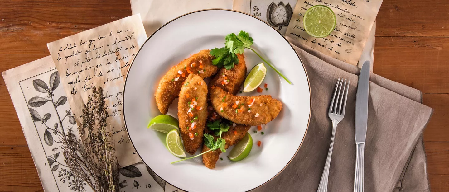 Filetes de pollo rebozados con lima y cilantro servidos en plato blanco