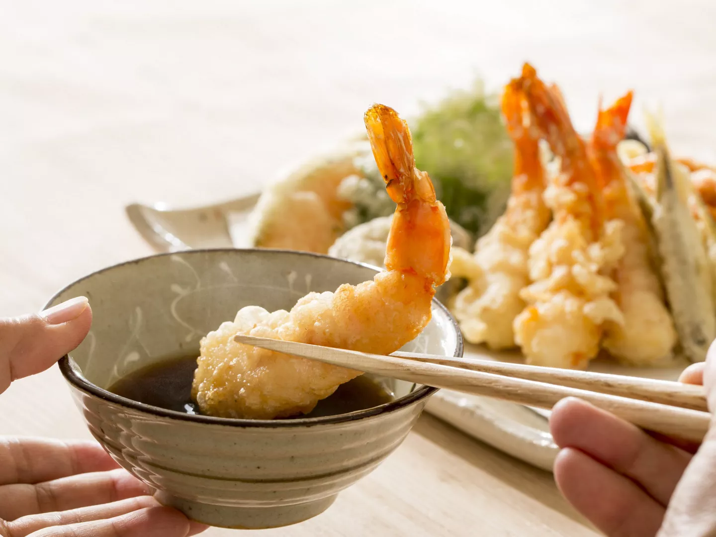 Manos sumergiendo tempura langostinos salsa soja