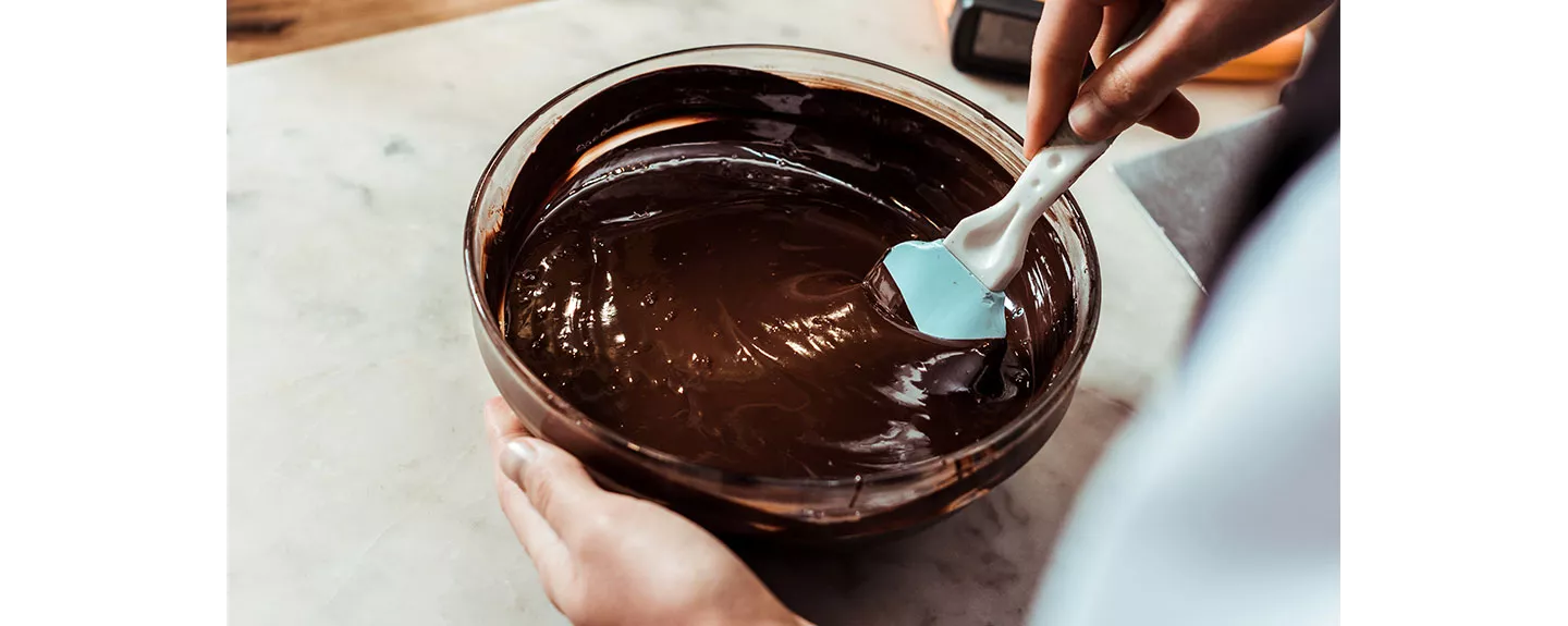 Una persona removiendo chocolate derretido en un bol para hacer praliné