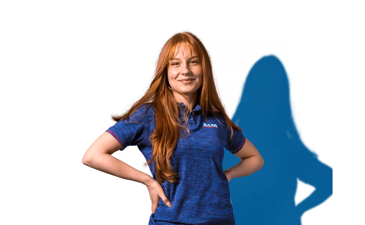 Eine Mitarbeiterin mit blauem Poloshirt steht mit den Händen in der Hüfte und lächelt in die Kamera.