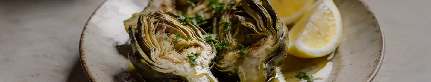 Alcachofas cocidas servidas en plato con limón y perejil 